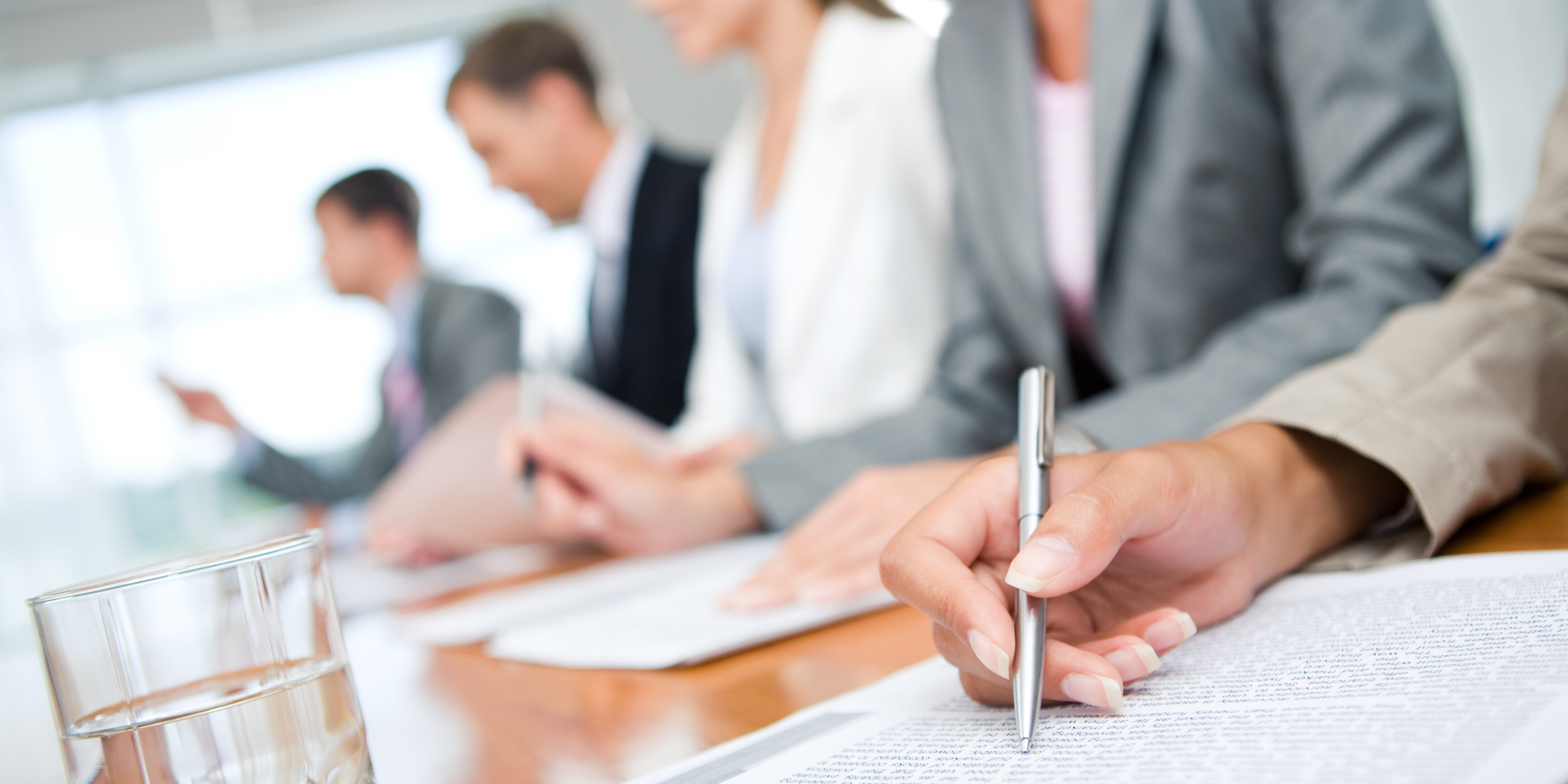 Close-up of womans hand with pen over document on background of business group